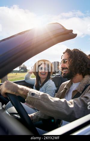 A young cheerful Caucasian couple driving in a convertible car enjoying the freedom of weekend trip Stock Photo