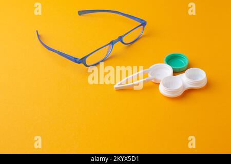 Glasses and accessories for contact lenses: a container for lenses and tweezers on a yellow background. Stock Photo