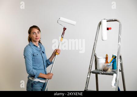 Women holding a paint roller for coloring walls, ladder with paint brushes and tools. Home improvement concept. Stock Photo