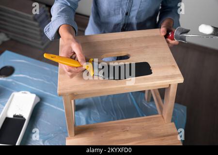 Young women preparing to restore a stepladder for children as a hobby house improvement. Pouring paint into a bucket on a table. Stock Photo