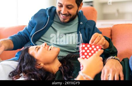 Young couple relaxing at new home, lying on the couch and eating popcorn. Stock Photo