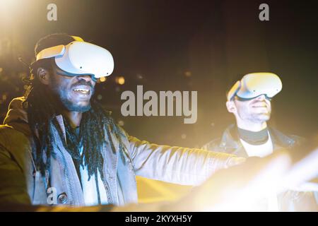 Two excited friends using VR glasses outdoor experiencing virtual reality adventure Stock Photo