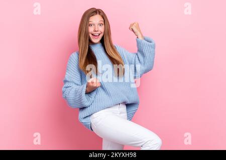 Photo of funky joyful schoolgirl wear blue knitted sweater fists up excited love her victories first place tournament isolated on pink color Stock Photo