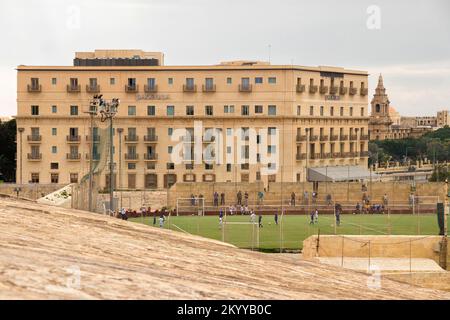 Valletta, Malta - November 12, 2022: 16th century fortification with a football pitch,  and view of Floriana town with Phoenicia hotel and St Publius Stock Photo