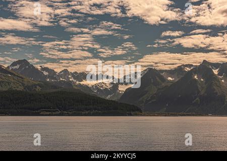 Seward, Alaska, USA - July 22, 2011: Wide landscape of Resurrection bay shoreline with snow covered mountain range and green forested flanks under blu Stock Photo