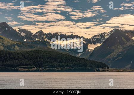 Seward, Alaska, USA - July 22, 2011: Green forested flanks from shoreline of Resurrection Bay of tall mountain range with show covered crevices and sh Stock Photo