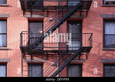 Close up New York City apartment building painted red brick exterior, windows, and diagonal fire escape stairs Stock Photo