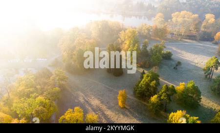Flight over the trees, glade, river in the park on a sunny autumn day. Aerial drone view. Autumn, fall season. Sunbeams. Beautiful natural background. Pink sun glare. Sunlight, shining sunbeams rays Stock Photo