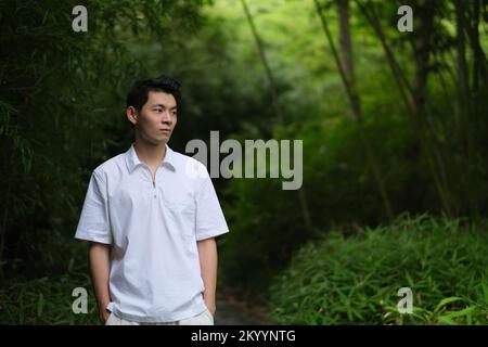 Handsome Asian young man at green bamboo grove, looking away Stock Photo