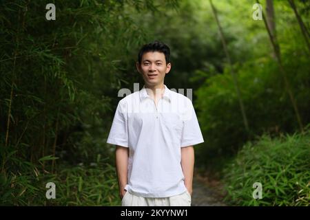 Asian young man at green bamboo forest, smiling at camera Stock Photo