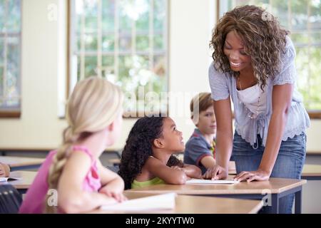 Well done. A young teacher spending some one-on-one time with her students during class. Stock Photo