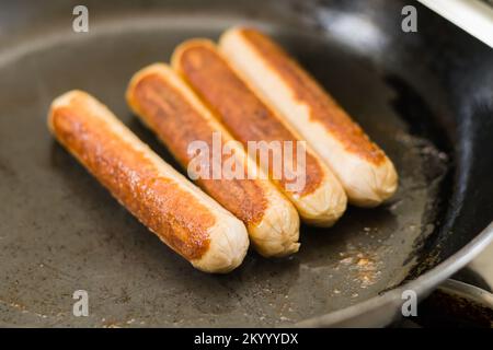 sausages being fried in a pan for breakfast. it is a staple breakfast food made of chicken, beef or pork.cold cut processed meat. Stock Photo