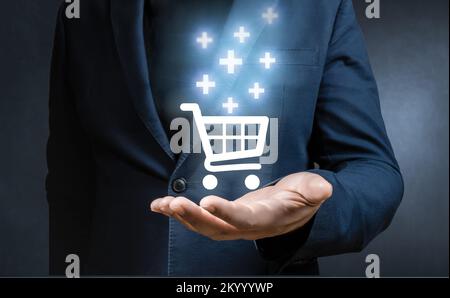 Sale volume increase. Businessman hand holding virtual trolley cart icons with plus sign symbol to add or receive an order. sale volume increase make Stock Photo