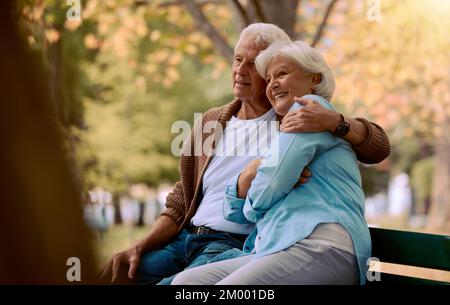 Couple, elderly and hug in park during retirement, sitting on park bench with love and spending quality time outdoor. Happy, trust and support with Stock Photo