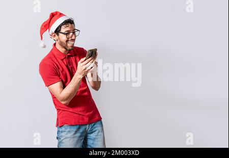 Smiling young man in christmas hat using cellphone isolated. Happy guy in christmas hat smiling at cellphone isolated. People in santa hat using and s Stock Photo