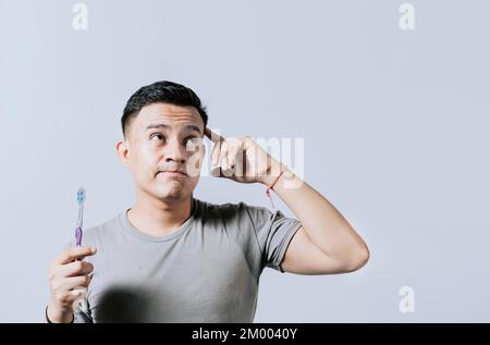 Man holding toothbrush with pensive expression isolated. Person holding toothbrush looking up, Thoughtful man holding toothbrush isolated, Portrait of Stock Photo