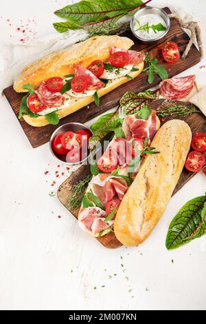 Two baguette sandwiches with salami, mozzarella cheese, lettuce, tomatoes and ham on a cutting boards. Long subway sandwiches on a white background. T Stock Photo