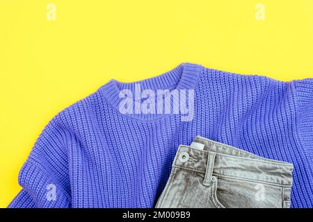 Purple sweater and gray jeans on yellow background. Casual women's outfit. Top view, flat lay. Stock Photo