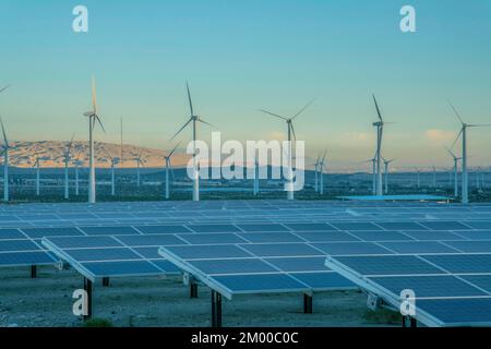 Desert wind farm near mountains with solar panels and wind turbines in California. View of solar panels and windmills during sunset and a background o Stock Photo