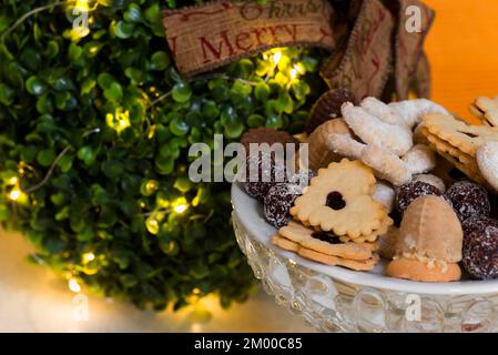 Small shining christmas tree sphere with ribbon "Merrry christmas" and many tiny traditional christmas cookies in glass bowl. Stock Photo
