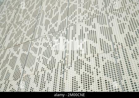 Low angle view of a beige metal wall sheet with decorative uneven holes. Building with metal wall sheets with decorative holes structure. Stock Photo