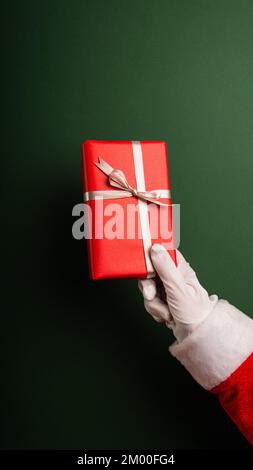 Cropped Santa's Hand Holding Gifts Against Green Background Stock Photo
