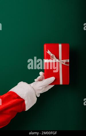 Cropped Santa's Hand Holding Gifts Against Green Background Stock Photo