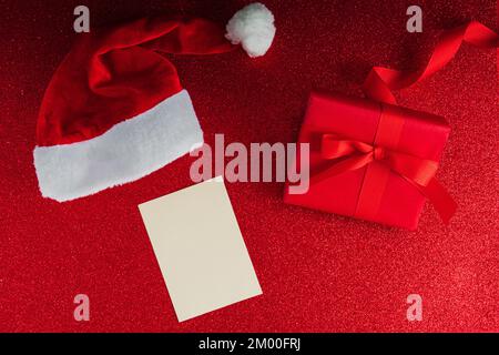 Santa Claus's hat with a luxury red present and a white postcard for mockup on glitter backdrop Stock Photo