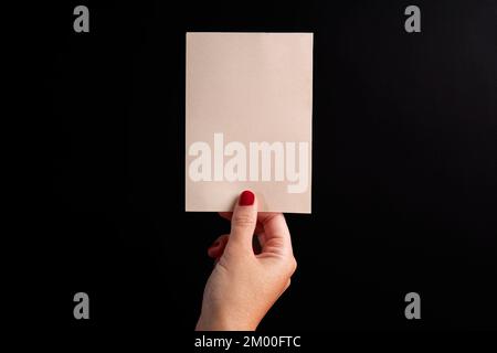 postcard in vertical format, held by a female hand on a black backdrop with copy space and mockup Stock Photo