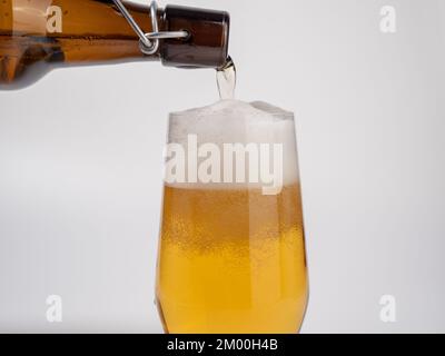 Fresh beer is poured from a bottle into a glass. Beer on a white background. Close-up. Stock Photo