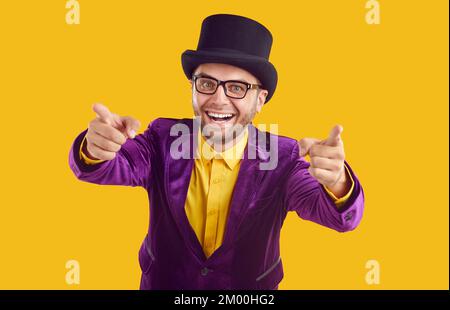 Happy unshaved showman in glasses is pointing index fingers on camera on beige background. Stock Photo