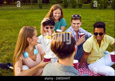Young positive group of friends men and women vacationers and laughing on picnic in park Stock Photo
