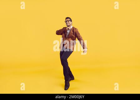 Funny young African American guy in a party jacket dancing on a yellow studio background Stock Photo