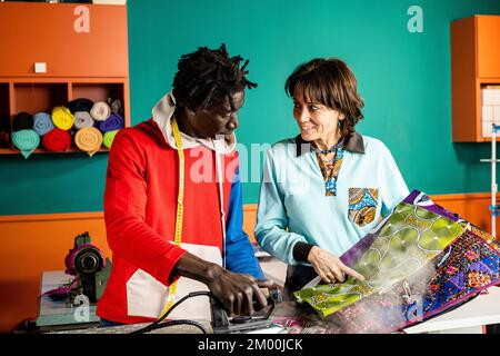 two tailors working on ideas and talking about projects, small business people working together in a hand made dress tailor workshop, concept of socia Stock Photo