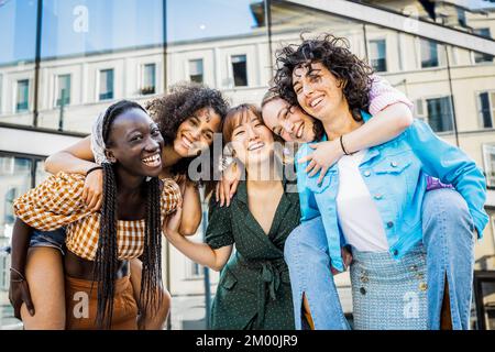 Portrait five friends women outdoor having fun hugging and riding piggyback, happiness, fooling around, togetherness concept, generation z people Stock Photo