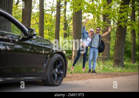 On the way to the city. Young people in the forest stopping the car and looking joyful.