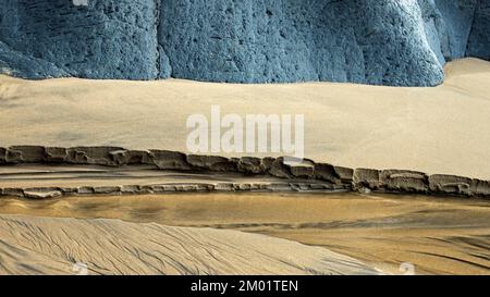Realistic abstract colour photograph of coastal rocks and sandy beach sculptured by the passages of time and tide with grained patterns and textures Stock Photo