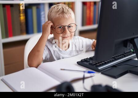 Adorable toddler student using computer sitting on table at classroom Stock Photo