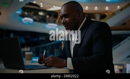 African middle-aged adult businessman worker entrepreneur man boss leader specialist company CEO freelancer teacher working with laptop writing notes Stock Photo
