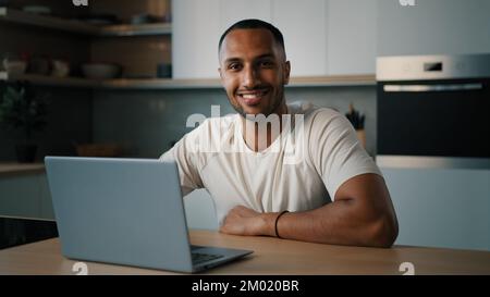 Smiling African millennial man guy American male user freelancer at home kitchen finish distant work with laptop satisfied with computer app online Stock Photo