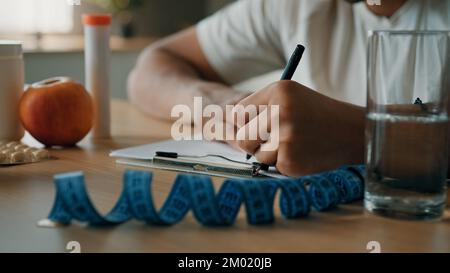 Close up male nutritionist unrecognizable man sport fitness trainer sitting at table writing prescription healthy nutrition fitness diet on paper Stock Photo