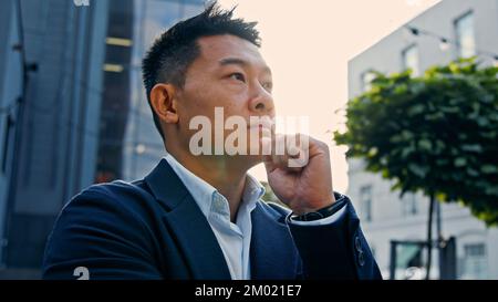 Dreaming alone thinking pensive 40s Asian Korean man puzzled confused thoughtful decision problem solution. Adult Chinese businessman entrepreneur Stock Photo