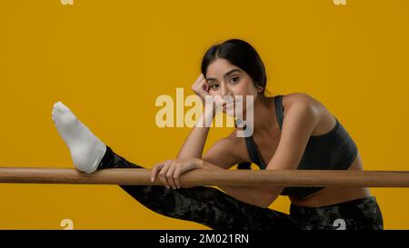 Indian sporty woman ethnic girl athlete female dancer ballerina lady in yellow studio trying stretching with ballet barre difficult problem with Stock Photo