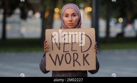 Sad muslim woman in hijab standing outdoors islamic ethnic girl upset unemployed worry stressful lady poor female showing holding cardboard banner Stock Photo