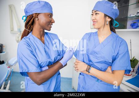 Two female doctors talk in a clinic during work, colleagues of different ethnicities Stock Photo