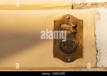 Close-up of a brass intercom with two doorbells on a yellow and white wall  with copy space, Italy, Europe. Stock Photo