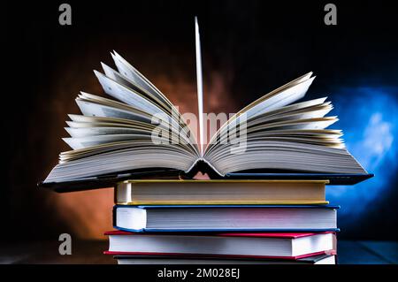 A composition with an open book lying on a stack of other books Stock Photo
