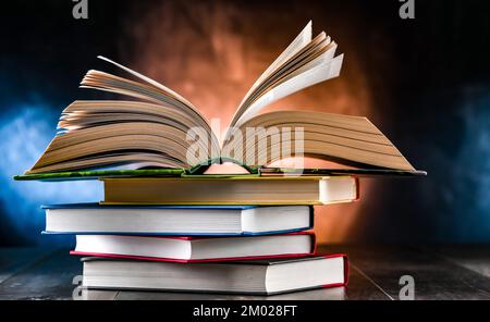 A composition with an open book lying on a stack of other books Stock Photo