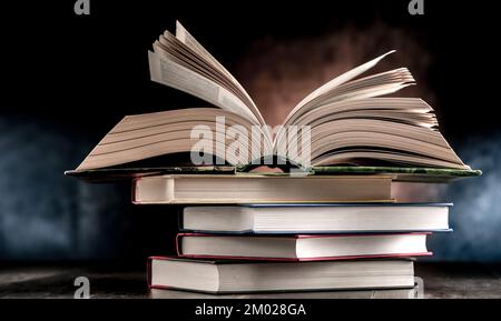 A composition with an open book lying on a stack of other books Stock Photo