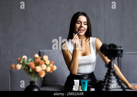 Vlogger female applies lipstick on lips. Beauty blogger woman filming daily make-up routine tutorial at camera on tripod. Influencer blonde girl live Stock Photo